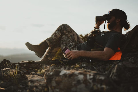 Man sits on mountain top and looks through binoculars.