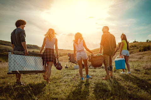 Group of young people carry chairs, cooler, and other personal items to the campsite.