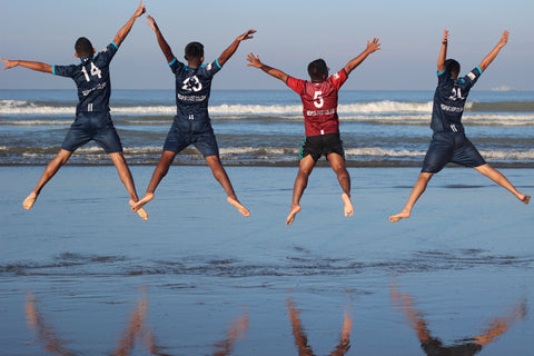 four men in soccer uniforms doing jumping jacks on beach 