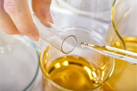 Glass pipette dropping golden oil into a glass beaker.