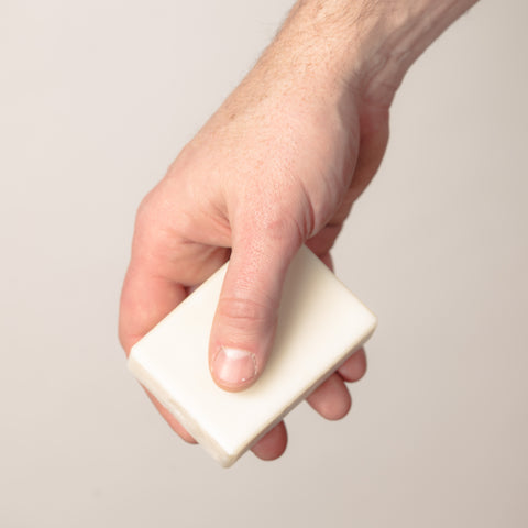 A man's hand holding a white bar of soap. 