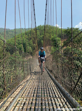 Roz Groenewoud cycling across a rickety bridge in Nepal. 