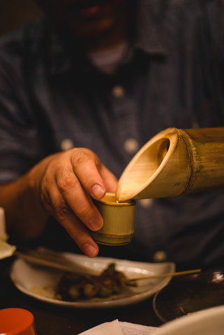 man pouring water from Bamboo shoot into cup made from bamboo shoot
