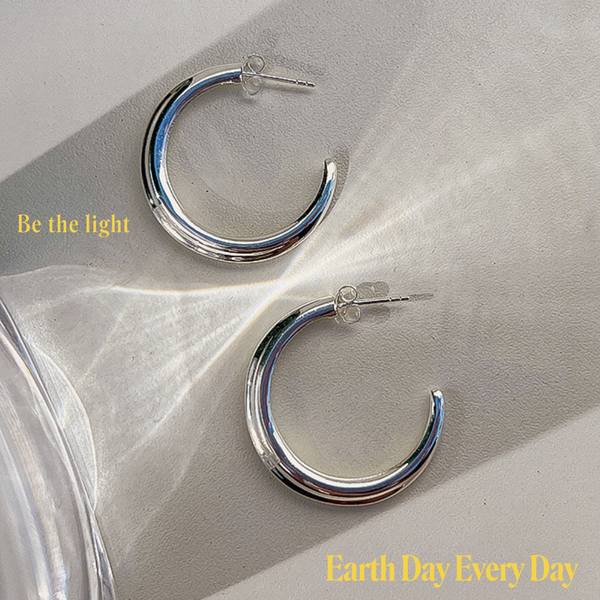 Modern SIlver hoop earrings with reflected light on a white back  ground.  In yellow words the text says " Be the light" and "Earth Day Every Day