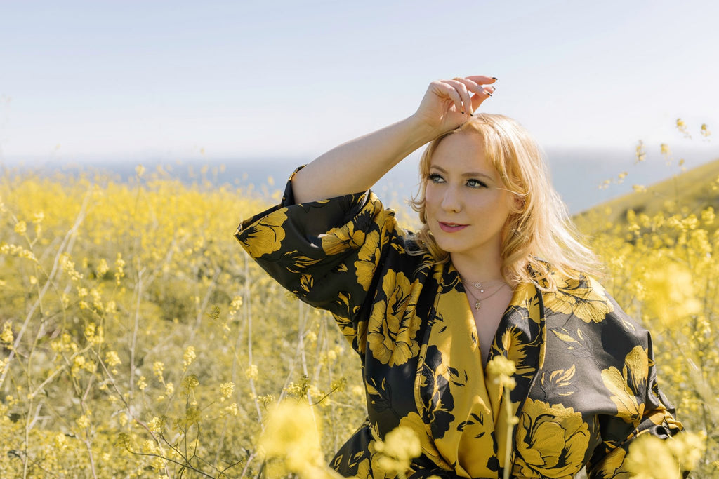 Kat eves for the Curvy fashionista wearing Astro & Orion good luck charm necklace and black dress in a field of yellow flowers.