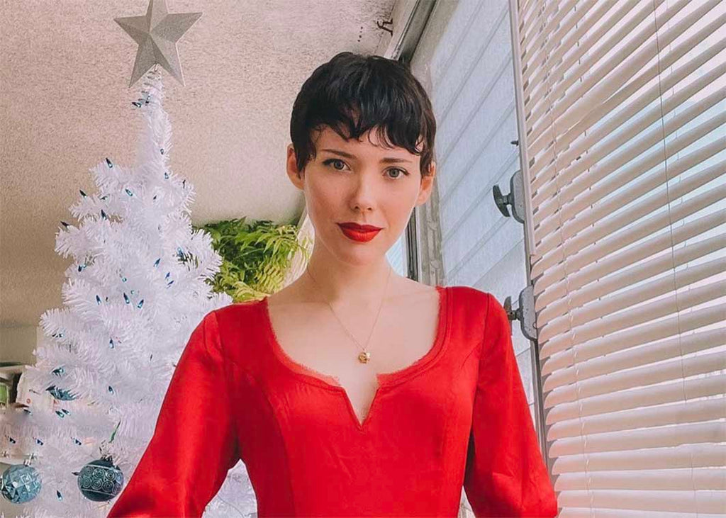 Sustainable Fashion Blogger The Style Theorist wearing a red dress, gold charm necklace standing in from of a white Christmas tree.