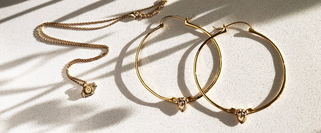 Astor + Orion ethically made jewelry. Gold hoop earrings and eye protection charm pendant in sunlight