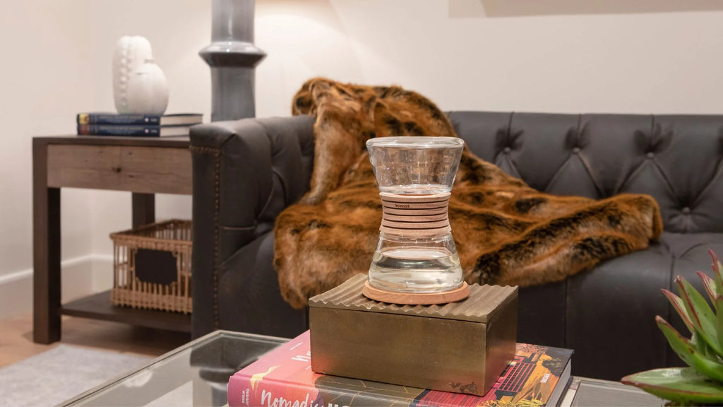Hyascent hourglass fragrance diffuser on a wooden crate on a coffee table with a black leather tufted couch with faux fur blanket.