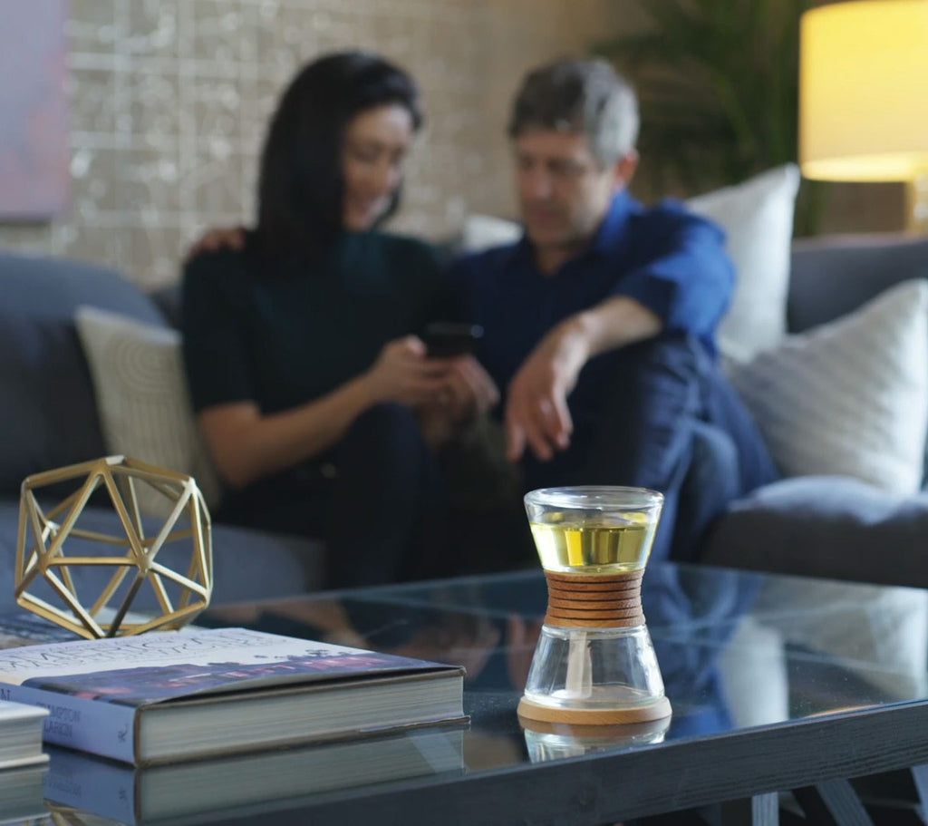 two people sitting on the couch looking at their phone, while a Hyascent hourglass fragrance diffuser sits in front.