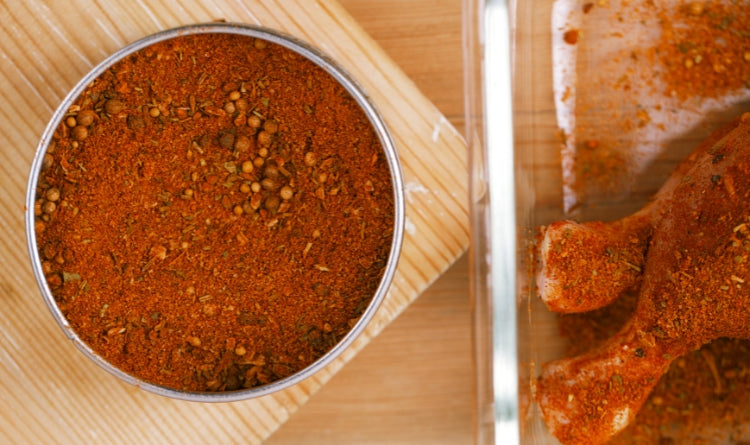 how to make sweet and spicy bbq rub. image showing orange bbq rub in a bowl next to seasoned chicken
