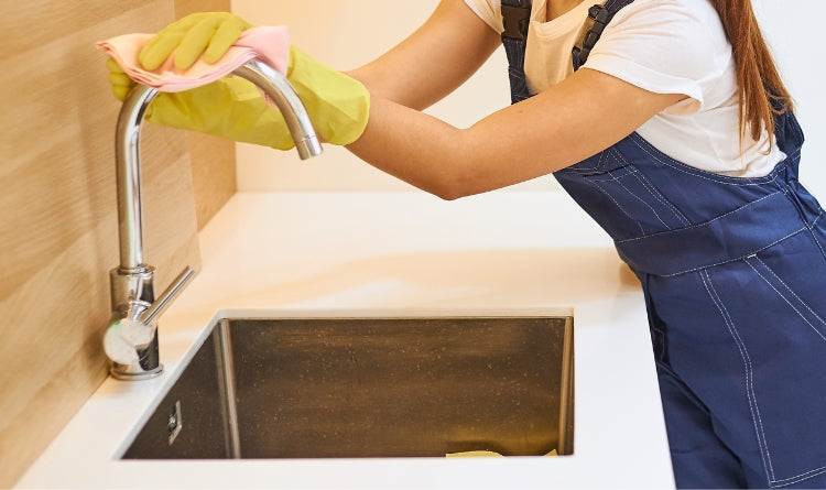 5 Ways to Clean Stainless Steel with Ingredients You Already Have at Home image showing woman cleaning a stainless steel kitchen faucet