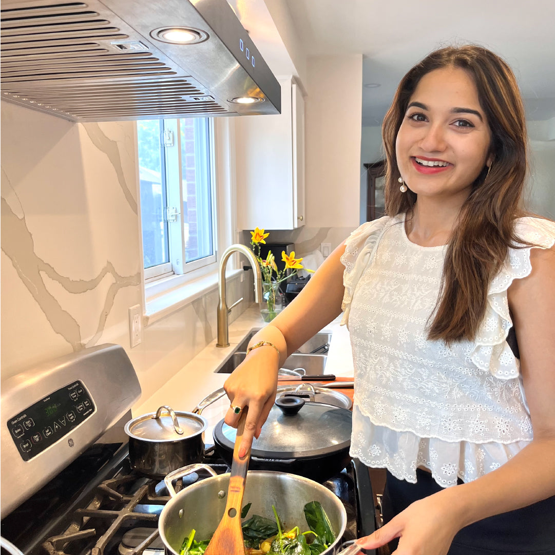 Disha Nayak posing next to her Hauslane Wm-530SS-30P wall mount kitchen range hood in stainless steel gray cooking palek paneer