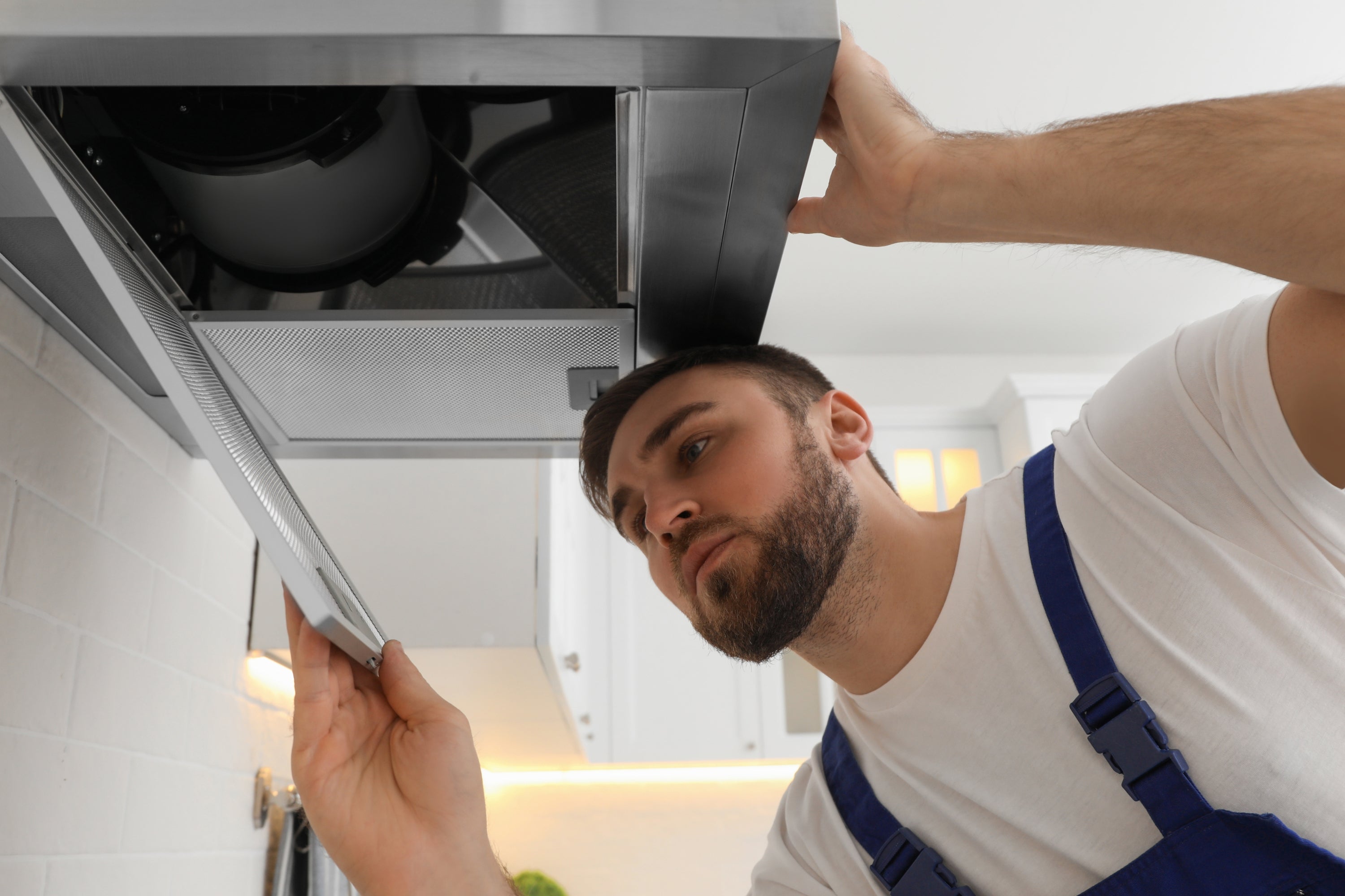 Solving Noisy Range Hood Cap Problems in Windy Conditions. Image showing a man looking at the underneath of a range hood with the filter open and the inside exposed