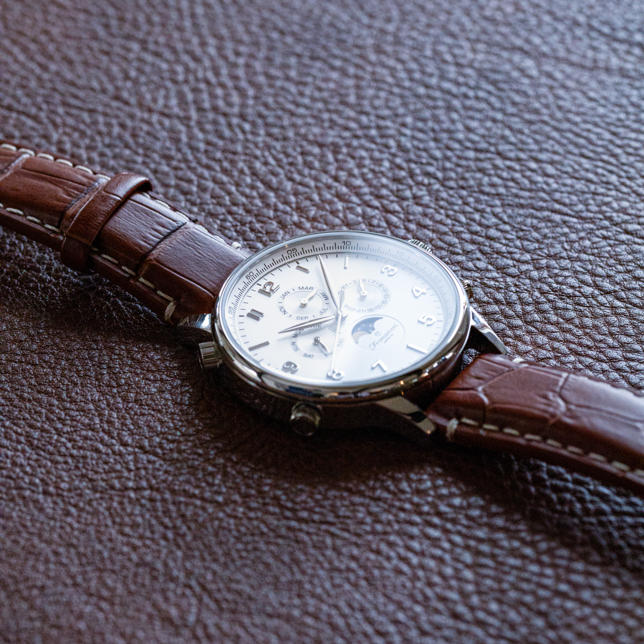 Photo of Fromanteel's iconic Moon Phase White watch with a brown leather strap laying flat on a matching brown leather surface.