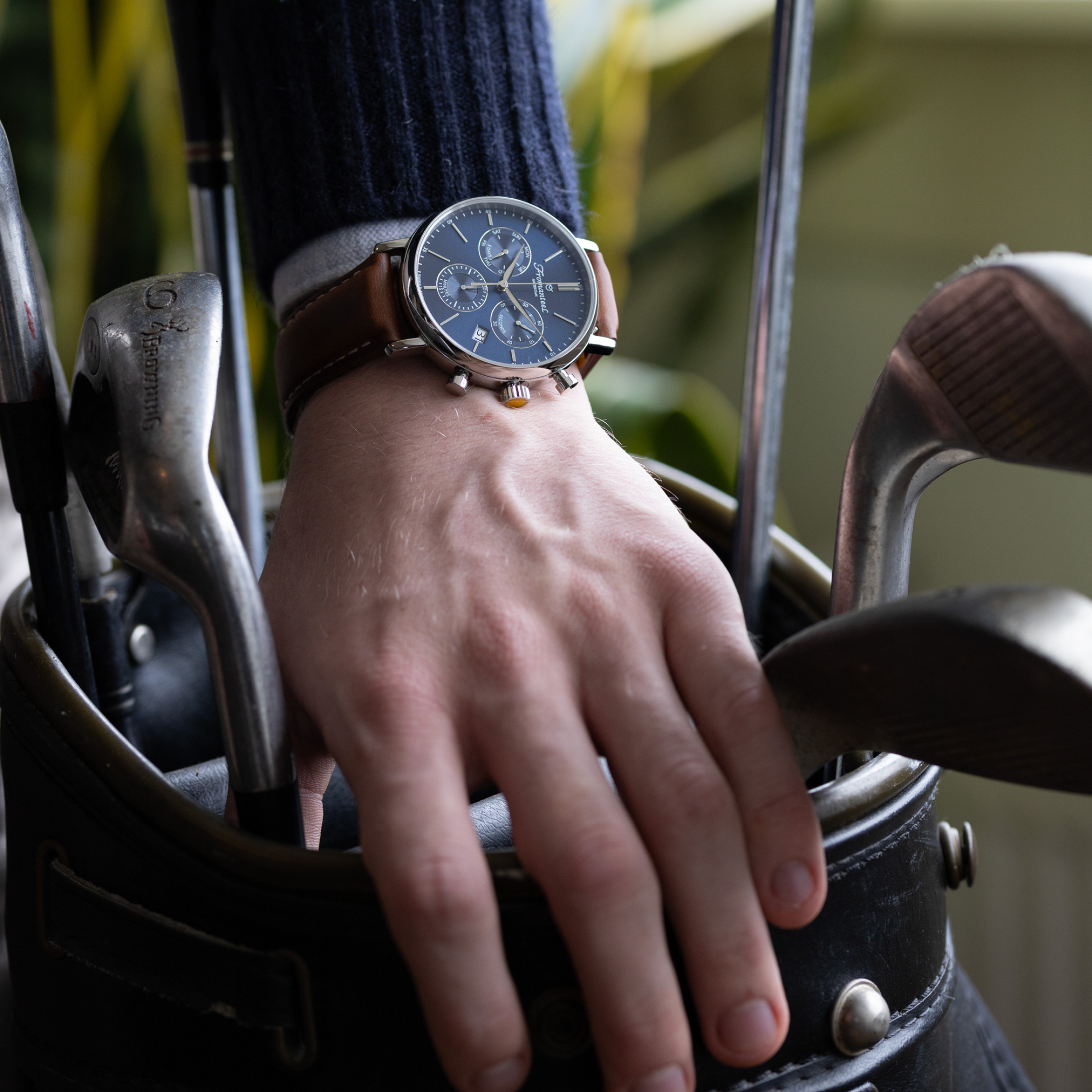 A photo of Fromanteel's Chrono Blue watch with a brown leather strap on a male wrist holding a golf bag.