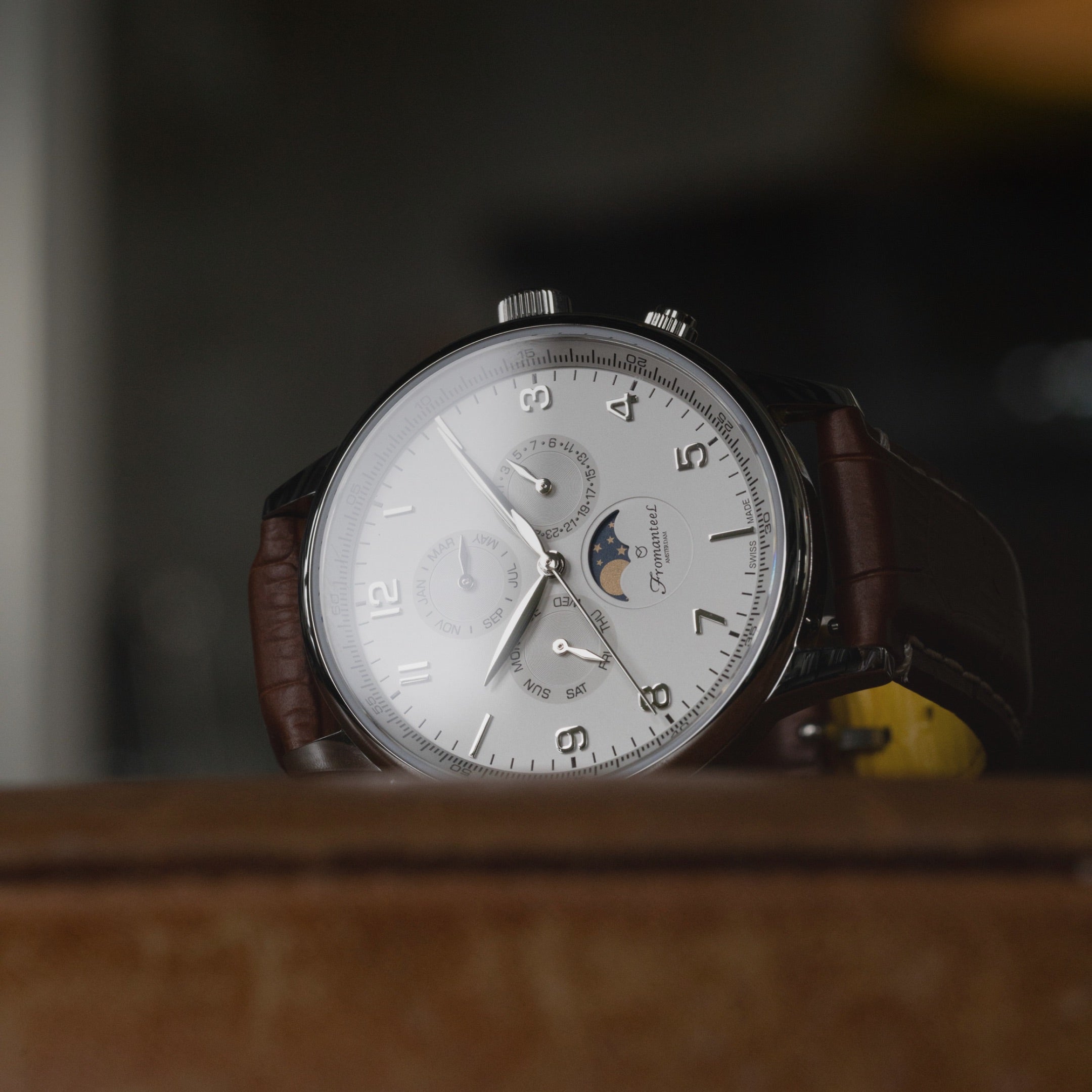 Photo of Fromanteel's iconic Moon Phase White watch with a brown leather strap laying flat on a matching brown surface.