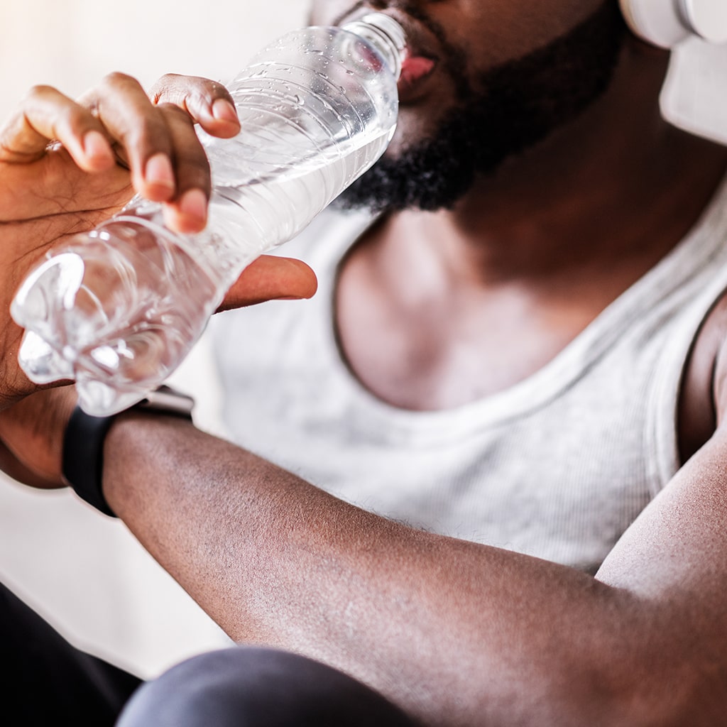 Close up of hands of young bearded athlete holding bottle of water.