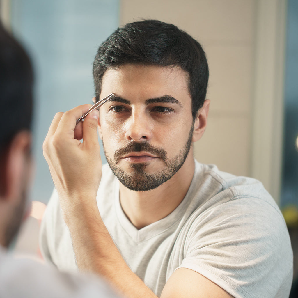 White metrosexual man trimming eyebrows with tweezers