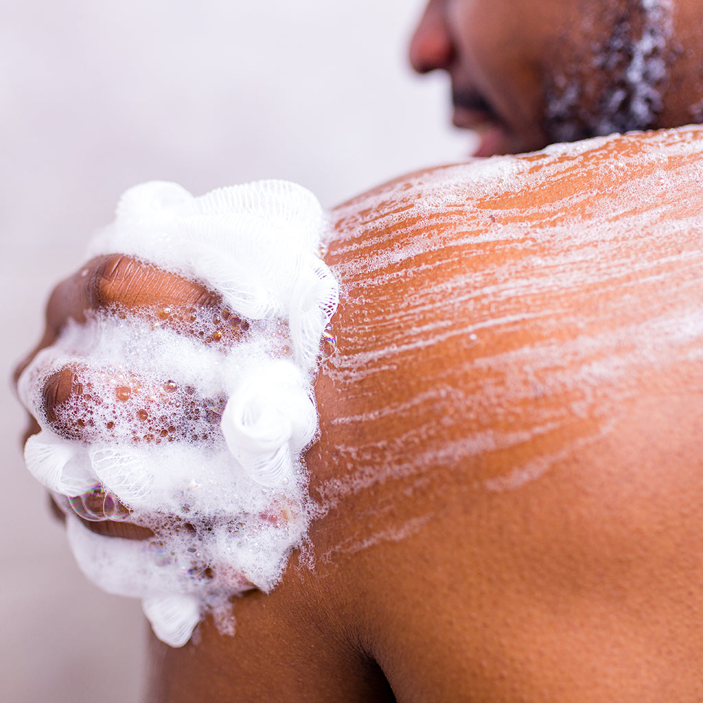 man washing body with shower sponge in white bathroom