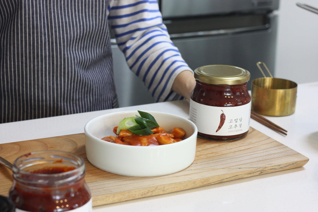 A person stands behind a cutting board with tteokbokki and gochujang on it