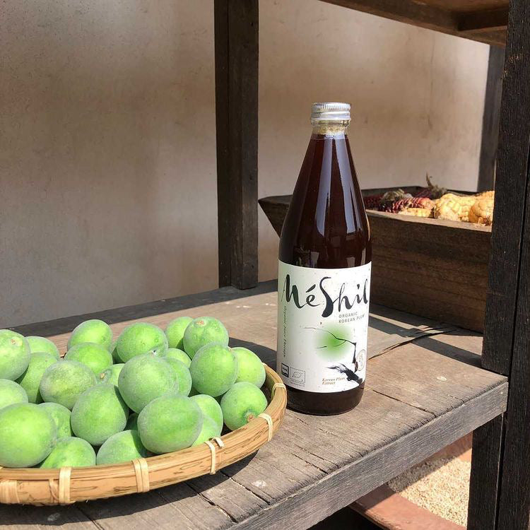 A bottle of maesil plum extract next to a basket of young green plums
