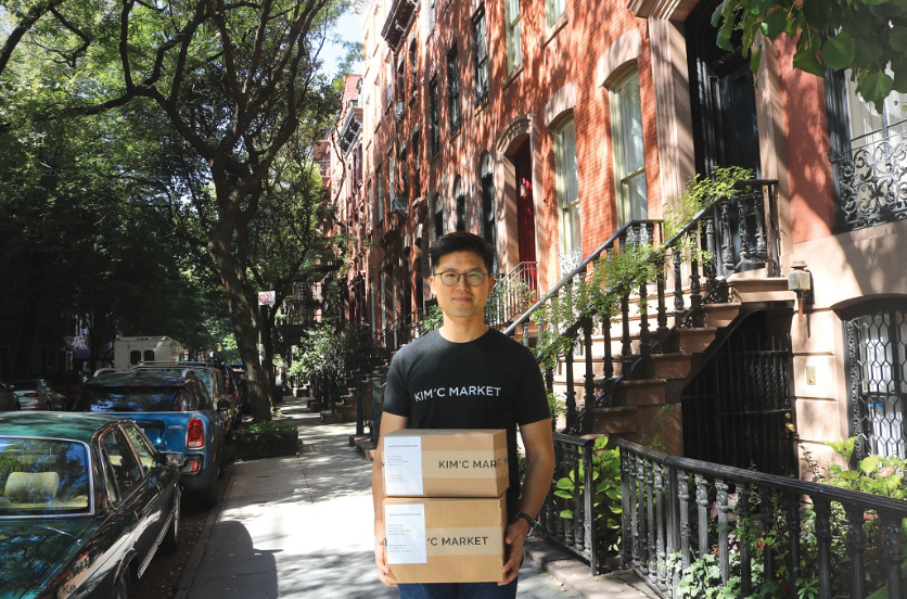 Ryan Kim holding Kim'C Market boxes on a street in a city