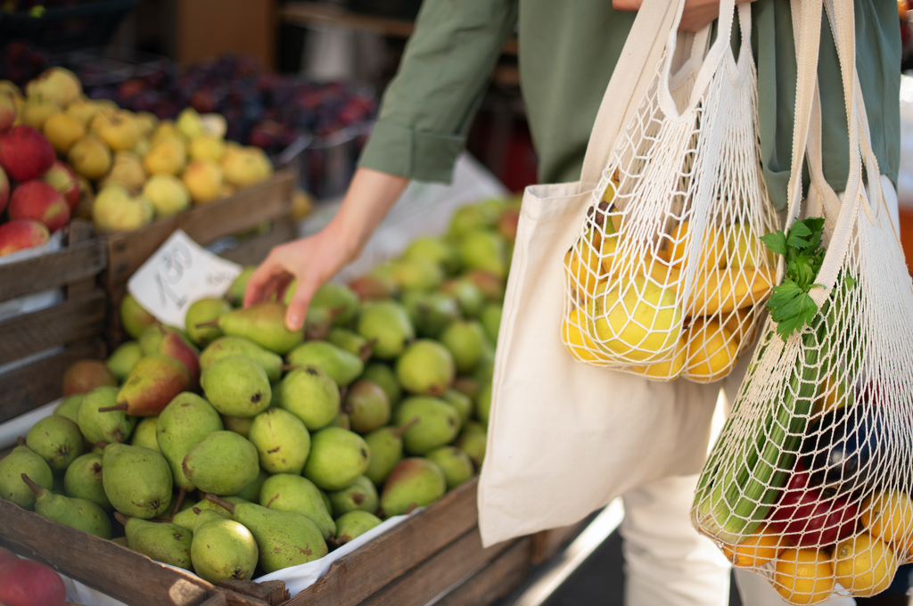 Someone shopping in the produce section of a grocery store with crocheted market bags