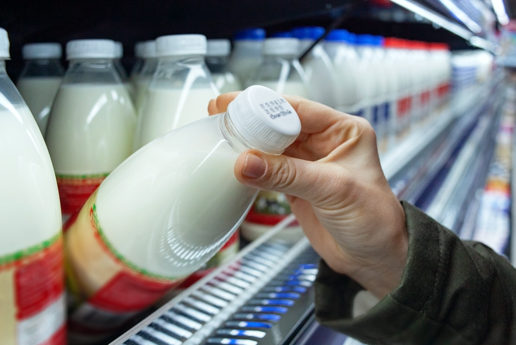 A milk bottle being taken off a shelf at a supermarket with a best-by date on the cap