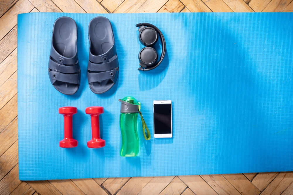 slippers earphones dumbbells and other gym stuff on a blue surface