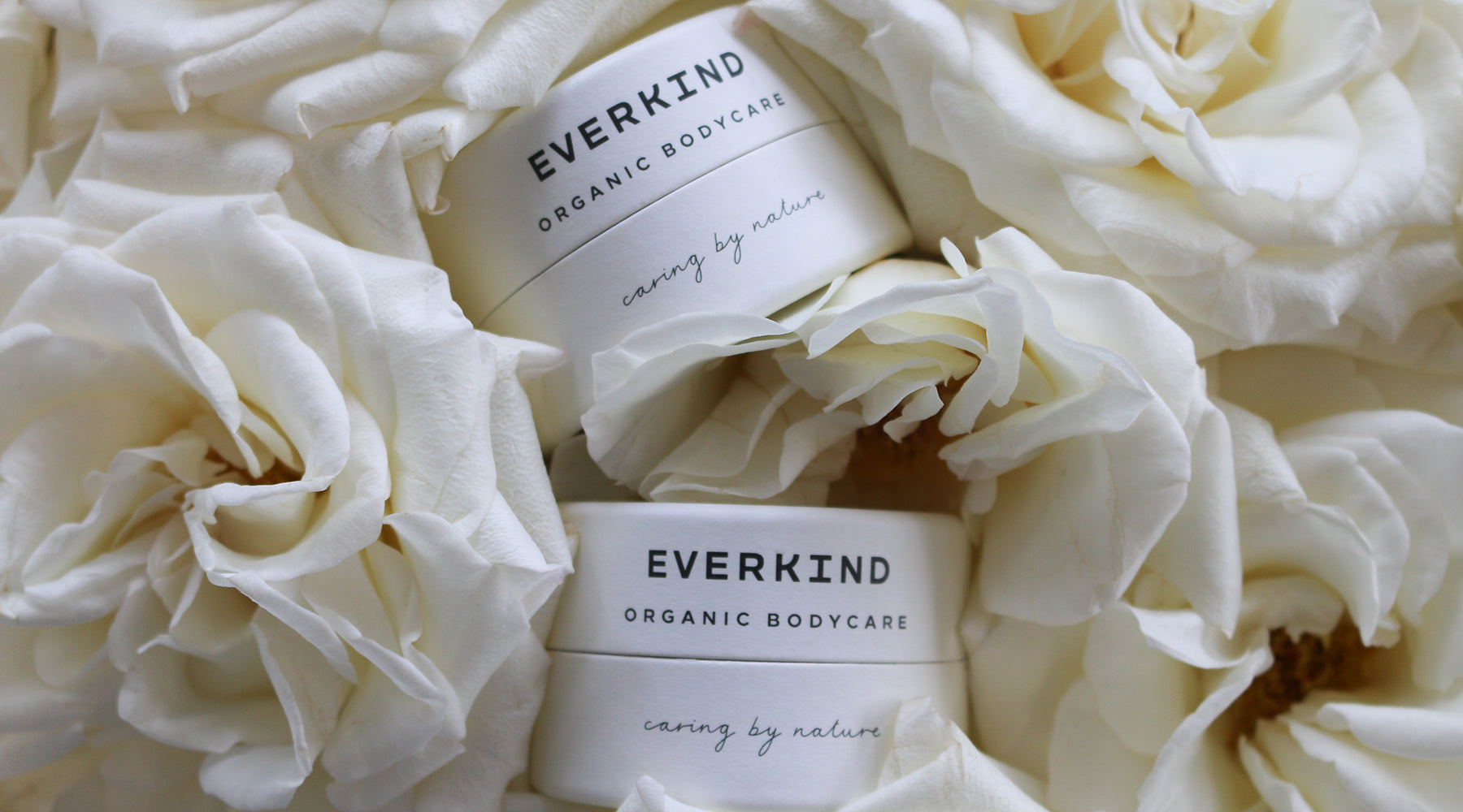 Photo of Everkind's new home compostable jars surrounded by beautiful white roses.