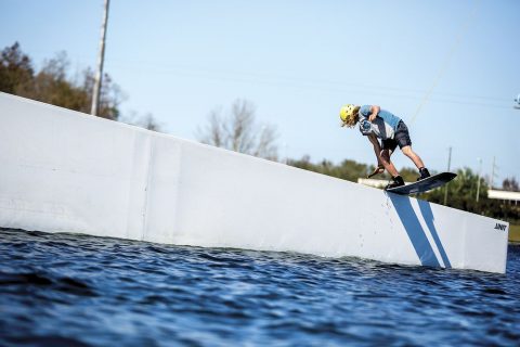 man with helmet performing a wakeboard trick on a wall in the water