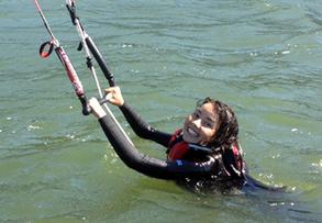 smiling female holding onto kiteboarding bar in the water looking at the camera