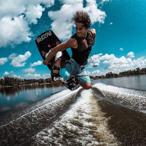 man with long hair performing a trick on a wakeboard above the water