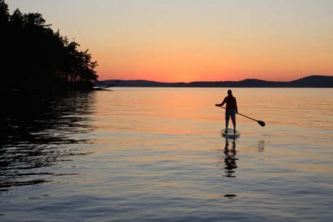 silhouette of a person paddle boarding on the water with a sunset in the background