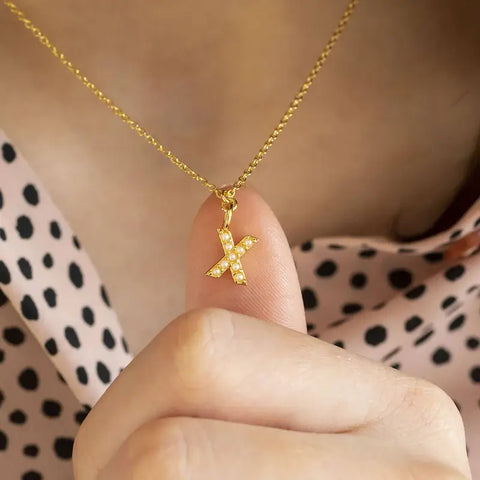 Image shows dainty pearl kiss necklace, a tiny 'X' encrusted with pearls on a gold plated trace chain.