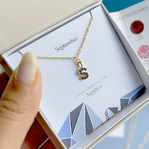 Image shows boxed initial birthstone necklace in september sapphire with the letter 's'