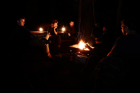 Friends of Ginew sit around a campfire at night. 