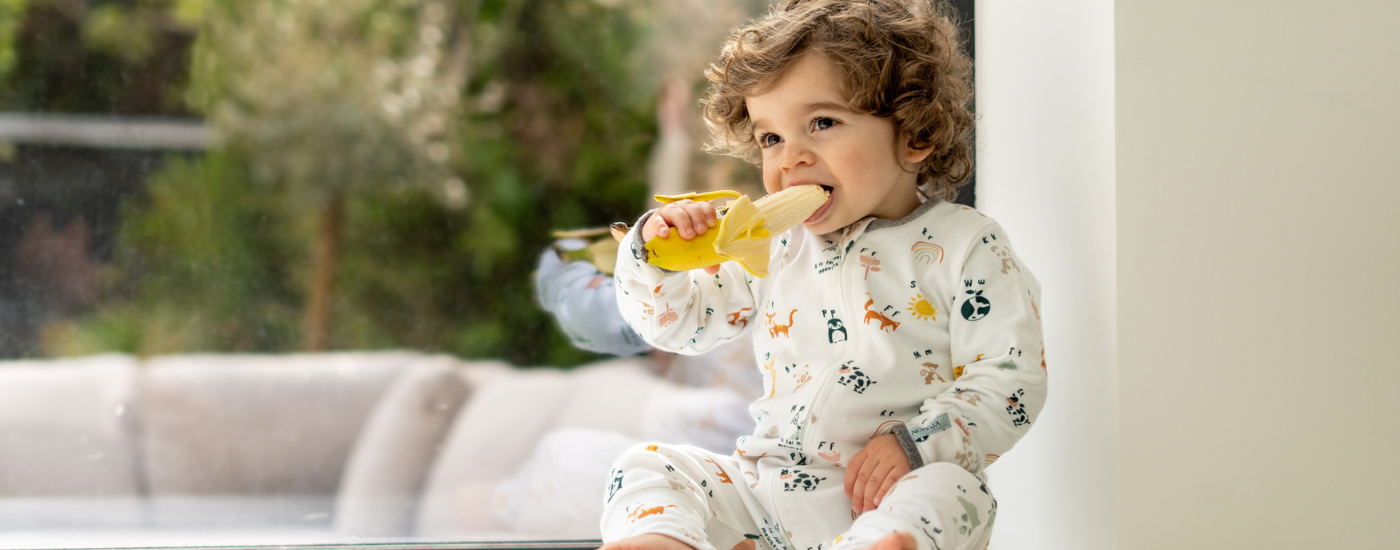 Baby in organic cotton onesie eating a banana