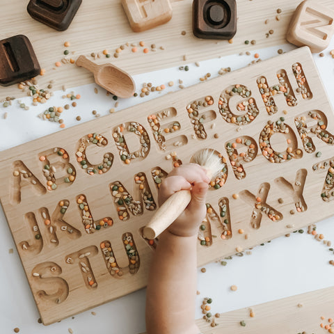 Wooden alphabet tracing board with a child filling in with sensory materials like rice and beans for sensory play.