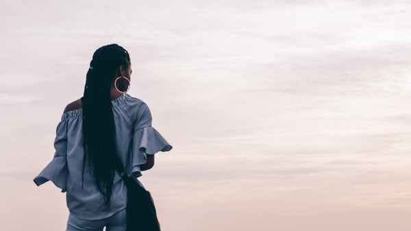 A woman relaxes, standing before a fresh white sky strewn with light clouds