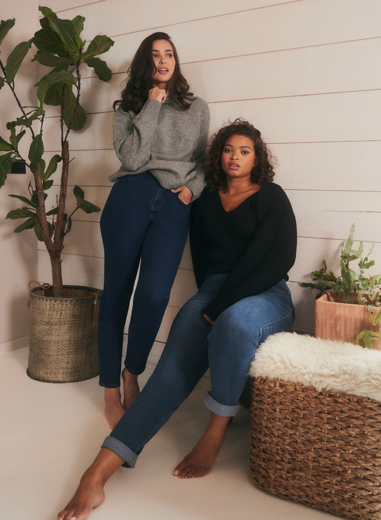 A curve Model sits on a chair, whilst a petite model stands. Both wearing the Straight Jeans by LOVALL.