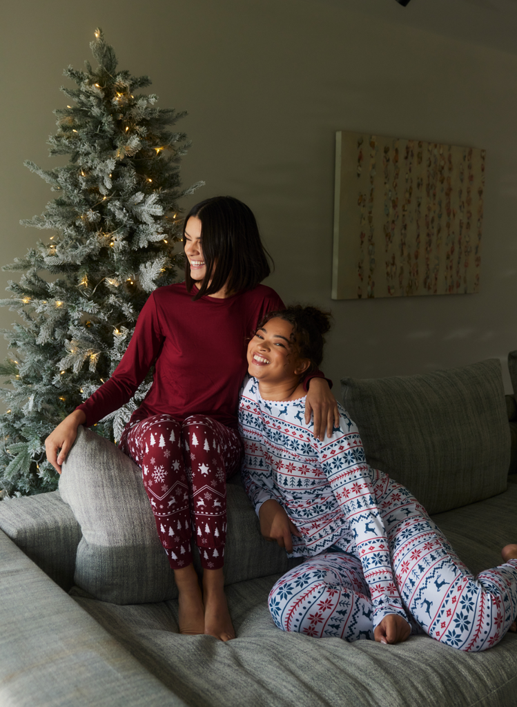 Women sit together on a sofa, in front of a Christmas Tree, wearing the Xmas Pyjamas by LOVALL.