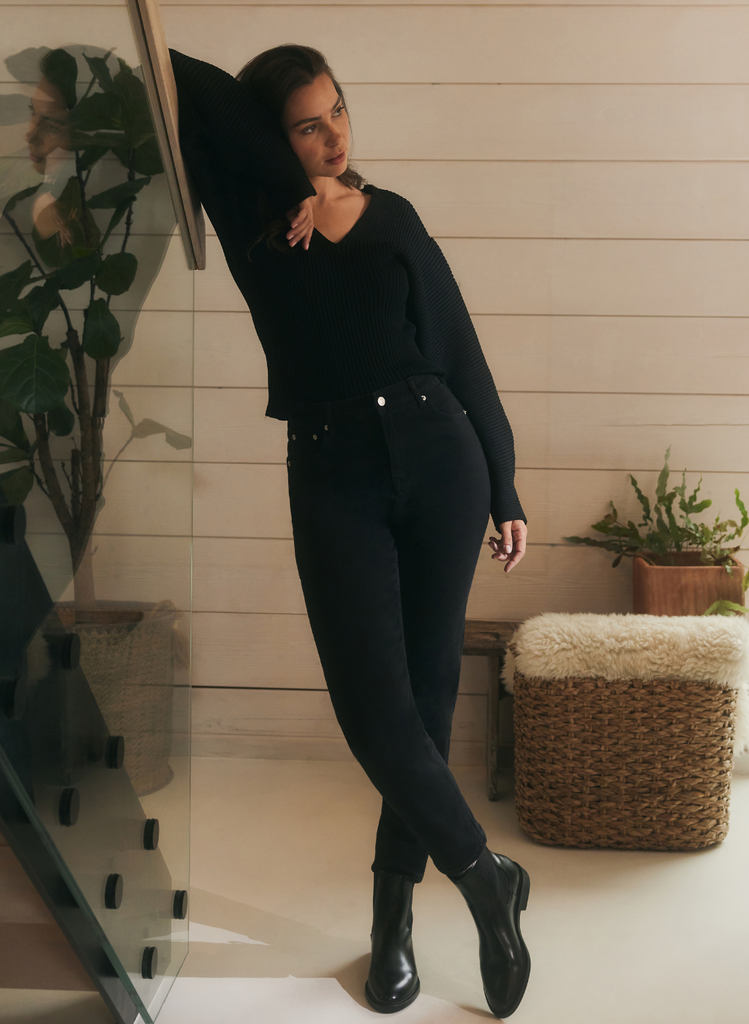 Woman wears the Black Mom Jeans, whilst stoo indoors leaning on a staircase.