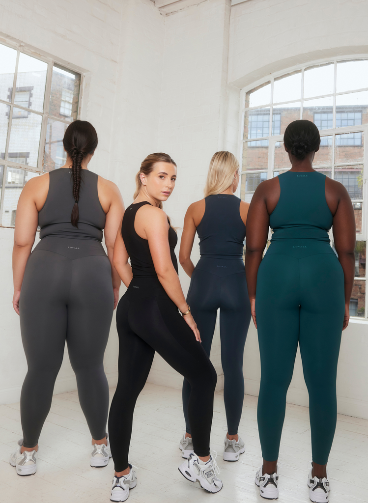 Dani Dyer wears the Black Empower Set, and stands with 3 models (facing away from the camera), wearing the Graphite Set, the Navy Set and the Deep Forest Set.