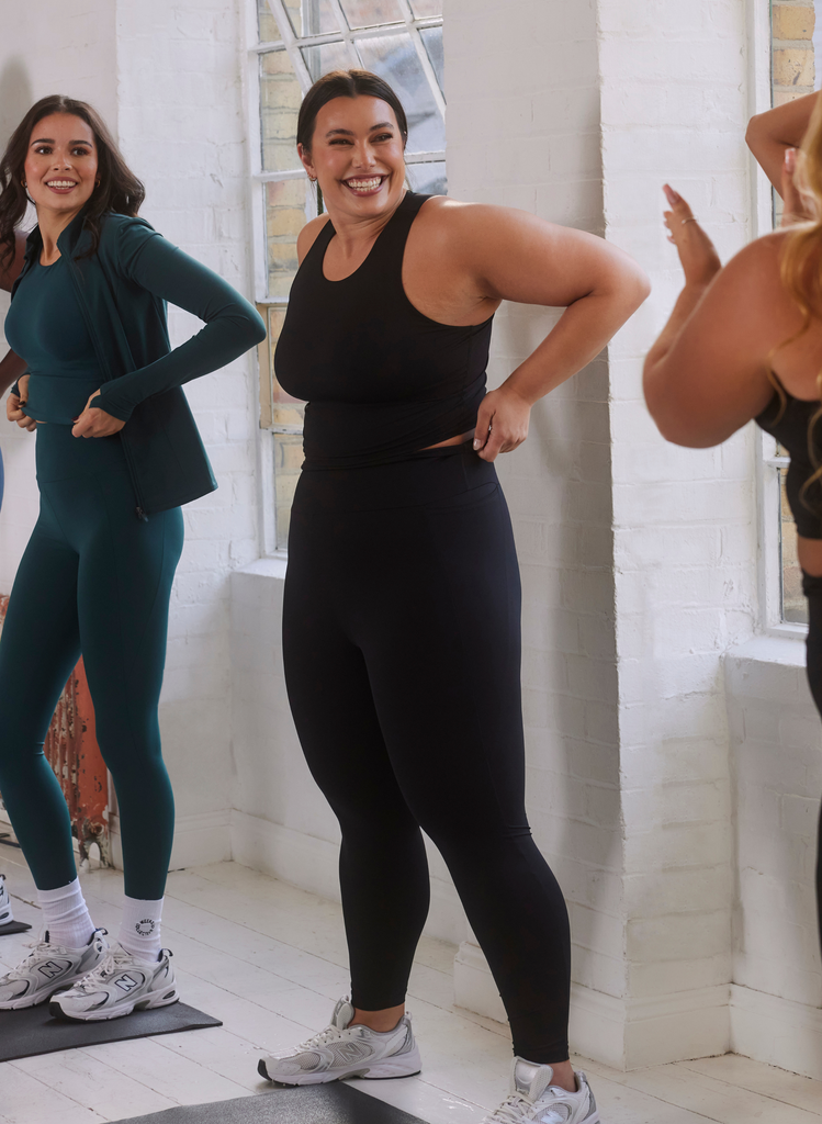 Woman wears the Black Empower Top and Leggings, she laughs with other women in a yoga class.