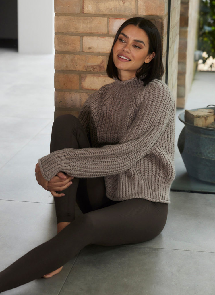 Woman sits on floor, wearing Ribbed Leggings and a knitted jumper.