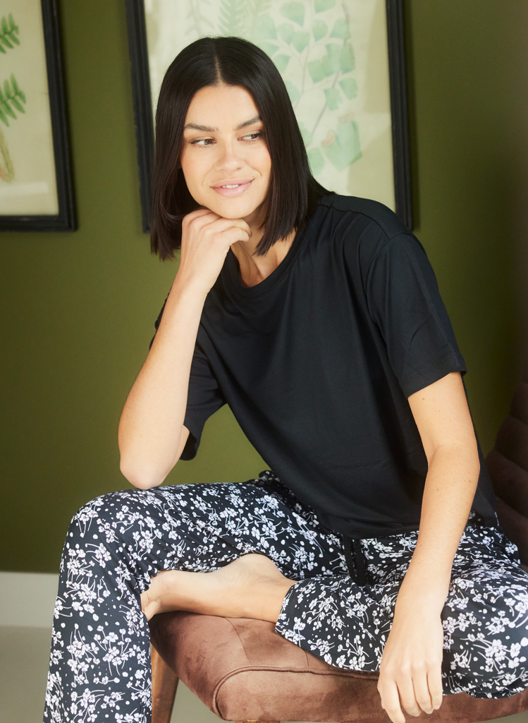 Woman sits on chair in the Black Floral Soft Touch Pyjamas.