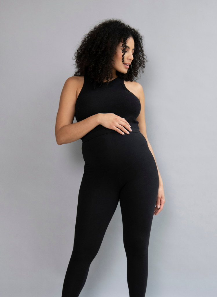 Woman wears Black Everyday Maternity Leggings with Black Tank Top. She stands against a studio backdrop.