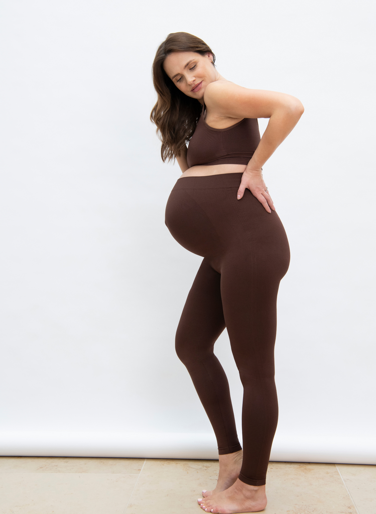 Woman wears Chocolate Brown Maternity Seamless Leggings with the matching Seamless Bralette. She stands against a studio backdrop.