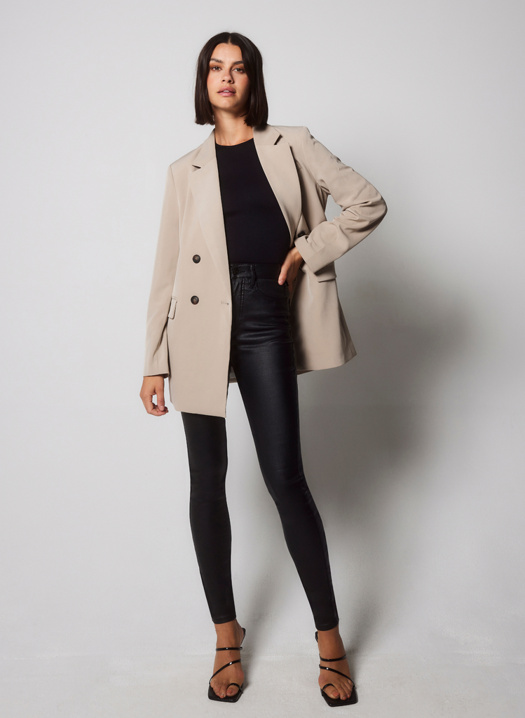 Woman wears Coated Jeans with black top and beige blazer.